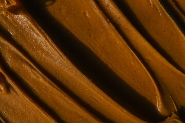 Close-up of smooth chocolate frosting with rich texture and deep brown color. The creamy, glossy surface has distinct swirls, highlighting its velvety consistency, perfect for cakes and desserts