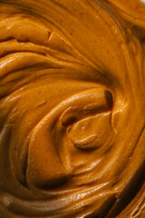 Close-up of creamy peanut butter spread with a rich, smooth texture. The golden-brown surface has...