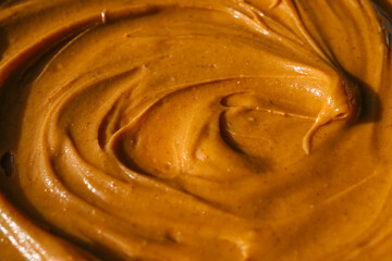 Close-up of creamy peanut butter spread with a rich, smooth texture. The golden-brown surface has...