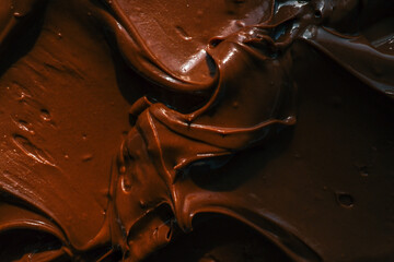 Close-up of smooth chocolate frosting with rich texture and deep brown color. The creamy, glossy surface has distinct swirls, highlighting its velvety consistency, perfect for cakes and desserts