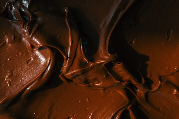Close-up of smooth chocolate frosting with rich texture and deep brown color. The creamy, glossy surface has distinct swirls, highlighting its velvety consistency, perfect for cakes and desserts