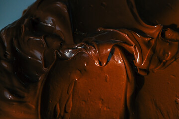 Close-up of smooth chocolate frosting with rich texture and deep brown color. The creamy, glossy surface has distinct swirls, highlighting its velvety consistency, perfect for cakes and desserts