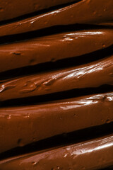 Close-up of smooth chocolate frosting with rich texture and deep brown color. The creamy, glossy surface has distinct swirls, highlighting its velvety consistency, perfect for cakes and desserts
