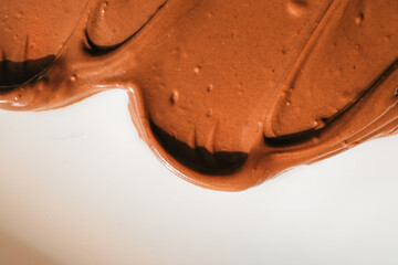 Smooth and glossy chocolate spread smeared on a white surface. The rich brown color and creamy texture highlight the indulgent nature of the sweet dessert ingredient, perfect for baking or spreading