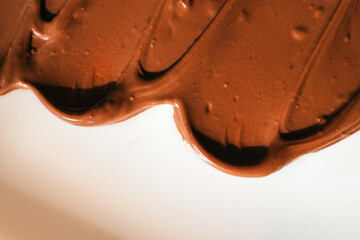 Smooth and glossy chocolate spread smeared on a white surface. The rich brown color and creamy texture highlight the indulgent nature of the sweet dessert ingredient, perfect for baking or spreading