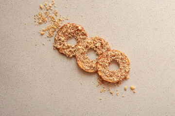 Three round dried apple slices with crushed nuts on top. Healthy organic fruit chips with nuts on beige background. Natural vegan dessert, minimal food composition, top view