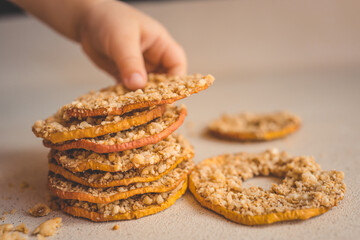 Child hand taking dried apple chip with crushed nuts. Healthy natural snack for kids, sweet fruit dessert with nuts. Organic sugar-free food for children. Close-up of hand and stack of chips
