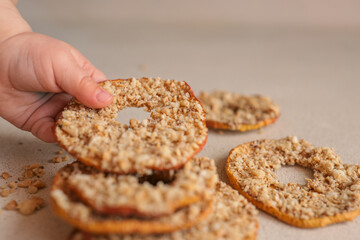 Child hand taking dried apple chip with crushed nuts. Healthy natural snack for kids, sweet fruit dessert with nuts. Organic sugar-free food for children. Close-up of hand and stack of chips