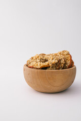 Wooden bowl with dried apple chips covered in crushed nuts on white background. Healthy organic snack, sugar-free vegan dessert, crispy fruit slices for diet and nutrition