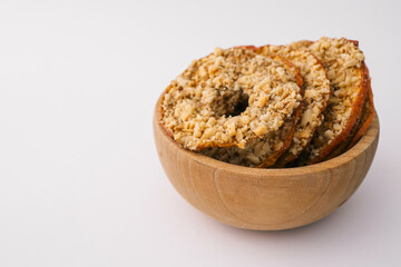 Wooden bowl with dried apple chips covered in crushed nuts on white background. Healthy organic snack, sugar-free vegan dessert, crispy fruit slices for diet and nutrition