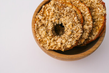 Wooden bowl with dried apple chips covered in crushed nuts on white background. Healthy organic snack, sugar-free vegan dessert, crispy fruit slices for diet and nutrition