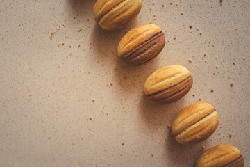 Traditional walnut-shaped cookies with cream filling, arranged in a row on a beige background....