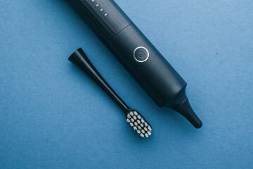 Black electric toothbrush with replaceable head on blue background. Modern rechargeable toothbrush for daily oral hygiene and dental care, minimalistic top view