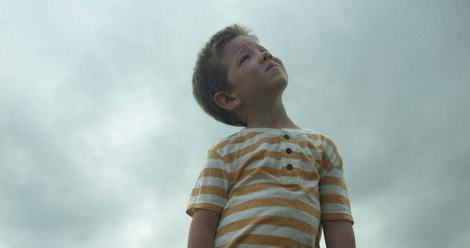 A child looks up to the sky with a dreamy expression, symbolizing curiosity, hope, and the search for meaning, watching the clouds.