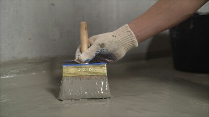 Professional construction worker applying liquid waterproofing membrane on concrete floor using...