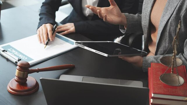 Two female lawyers in business suits meet at wooden desk, shaking hands over contract paper. wooden gavel and scales justice as discuss legal compliance, corporate law, dispute resolution.