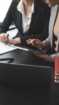 Two female lawyers in business suits meet at wooden desk, shaking hands over contract paper. wooden gavel and scales justice as discuss legal compliance, corporate law, dispute resolution.
