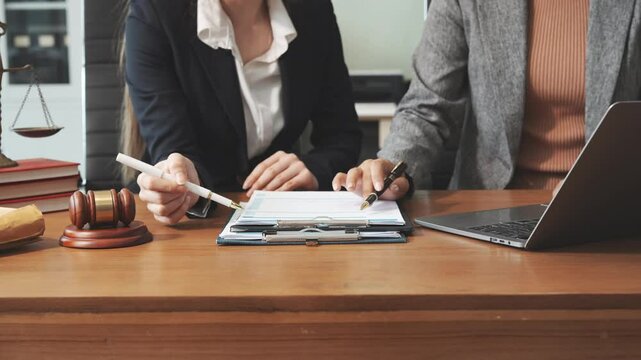 Two female lawyers in business suits meet at wooden desk, shaking hands over contract paper. wooden gavel and scales justice as discuss legal compliance, corporate law, dispute resolution.