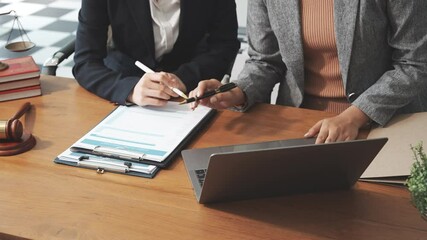Two female lawyers in business suits meet at wooden desk, shaking hands over contract paper. wooden gavel and scales justice as discuss legal compliance, corporate law, dispute resolution. - Powered by Adobe