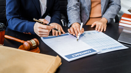 Two female lawyers in business suits meet at wooden desk, shaking hands over contract paper. wooden...