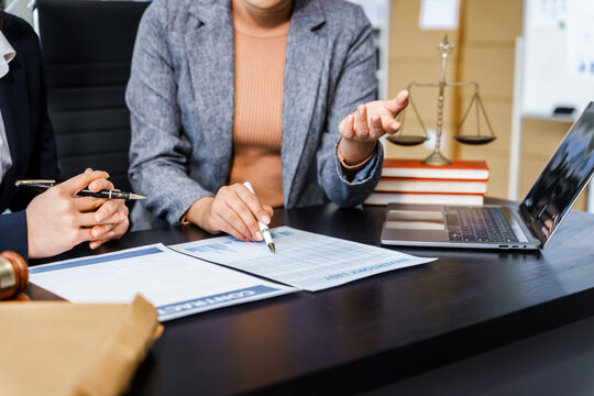 Two female lawyers in business suits meet at wooden desk, shaking hands over contract paper. wooden gavel and scales justice as discuss legal compliance, corporate law, dispute resolution.
