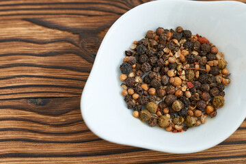 black and white peppercorns in a bowl on a wooden background