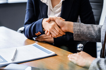 Two female lawyers in business suits shake hands at wooden desk, finalizing legal agreement. wooden gavel and scales represent justice as they discuss corporate law, compliance, dispute resolution.