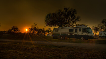 Sunburst on Rv motorhome at campsite with trees and road