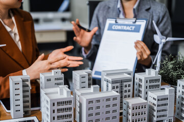 Two businesswomen sit at a desk in a meeting, discussing property development while building a...