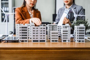 Two businesswomen sit at a desk in a meeting, discussing property development while building a...