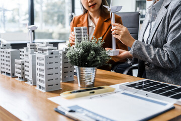 Two businesswomen sit at a desk in a meeting, discussing property development while building a...