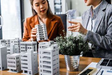 Two businesswomen sit at a desk in a meeting, discussing property development while building a...