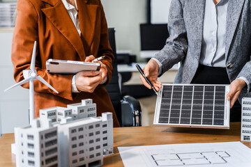 Two businesswomen sit at a desk in a meeting, discussing property development while building a...
