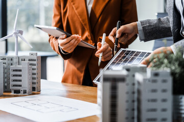 Two businesswomen sit at a desk in a meeting, discussing property development while building a...