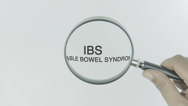 IBS (Irritable Bowel Syndrome) text highlighted by a magnifying glass in a hand on a white background, symbolizing focus on digestive health, symptoms, and management