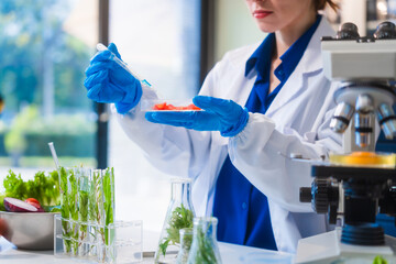 Middle-aged female laboratory worker wearing blue gloves conducts lab test on food ingredients...