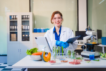 Middle-aged female laboratory worker wearing blue gloves conducts lab test on food ingredients lettuce, cucumber, pork. Using microscope, she analyzes nutrients, preservatives, food safety records.
