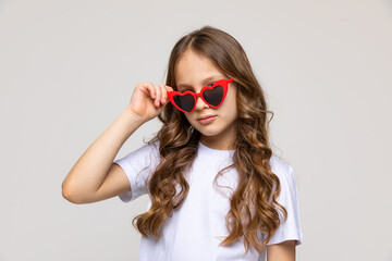 Photo of pretty cute little girl dressed white casual t-shirt and red heart-shaped sunglasses, white color background. Summer concept. Copy space
