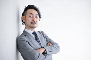 Smiling businessman leaning against a wall and folding his arms, looking at the camera