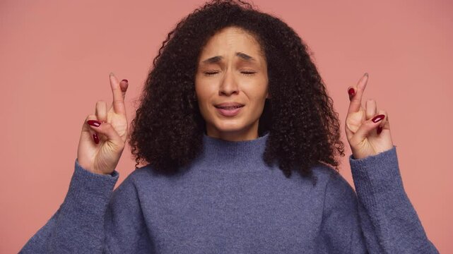 Hopeful woman crossing fingers for good luck on pink background