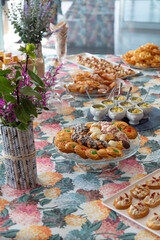 Table with a glass tray and tea cakes, glasses, and fruit cups. Floral tablecloth with hydrangeas. Eat, sweet, delicious.