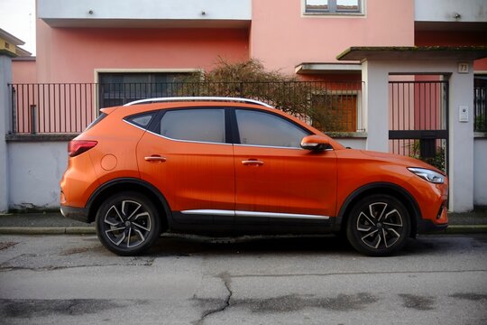 Side view of an orange MG ZS 1.0T GDI parked on a street in Cremona, Italy, showcasing its modern design