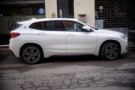 White BMW X2 parked on cracked asphalt, highlighting urban landscape of Cremona, Italy streetscape