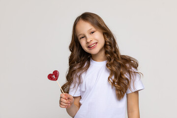 Happiness, childhood, kid and sweets. A happy little girl holding a heart shaped lollipop caramel...