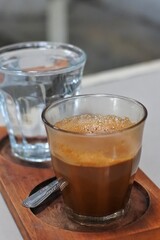 Close up of a glass of sanger coffee and water served on a wooden cutting board.