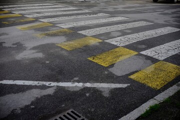 Worn pedestrian crosswalk displaying yellow and white markings on cracked asphalt street in...
