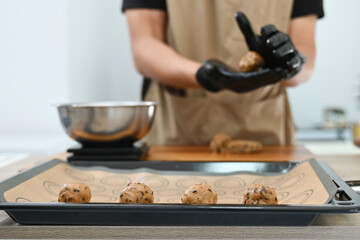 A man is making cookies and wearing gloves. He is using a scale to measure the ingredients. The cookies are on a baking sheet.