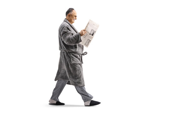 Man in a bathrobe walking and reading a newspaper