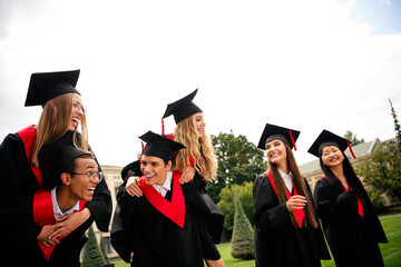 Joyful young graduates wearing mortarboards and gowns celebrate finishing their education outdoors...