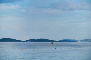 A boat glides across calm waters near distant islands, showcasing a peaceful coastal landscape under a clear sky.